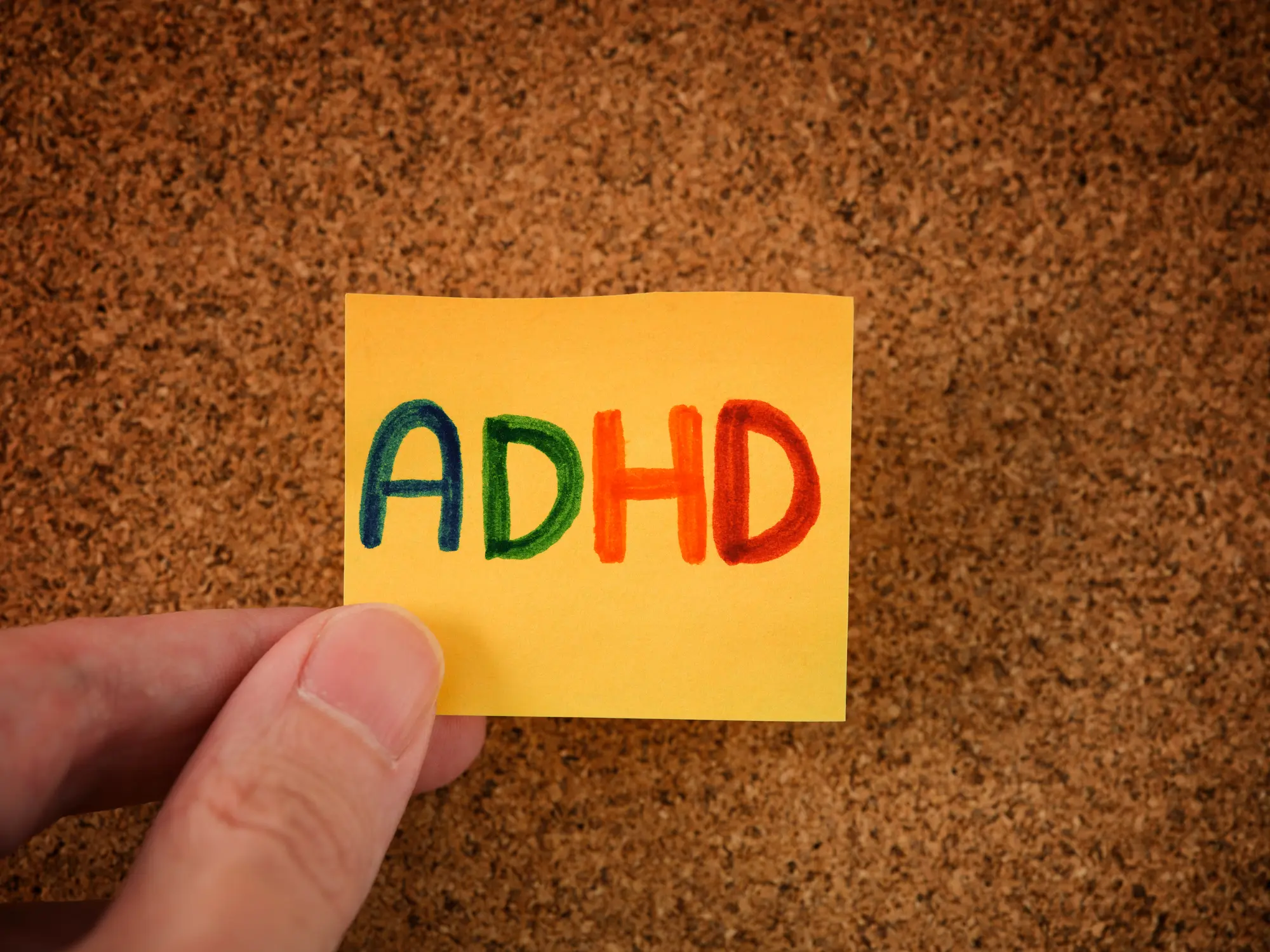 Hand holding a sticky note with 'ADHD' written in colorful letters.
