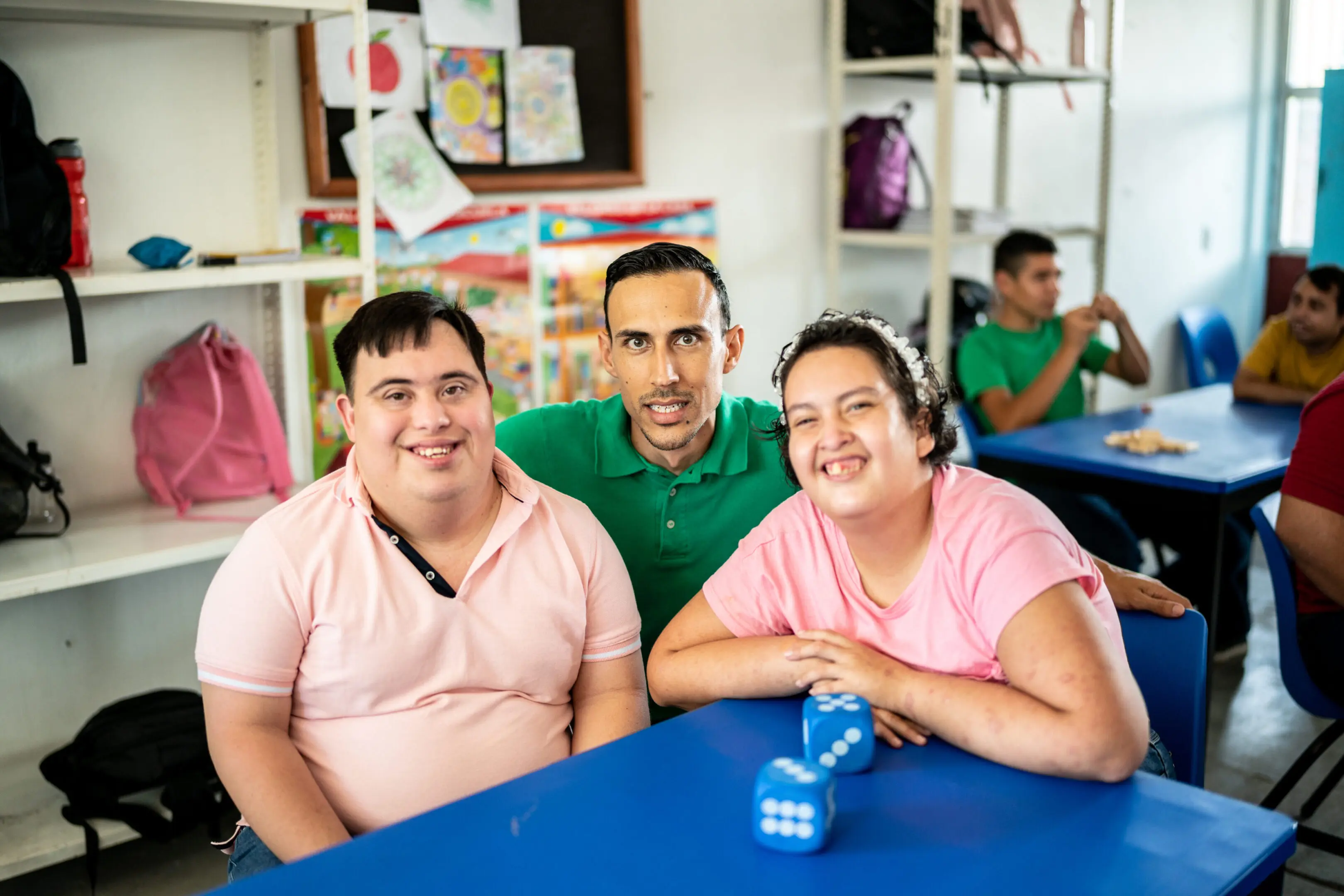 Three smiling friends sitting at a table with a blue surface and a small blue object.