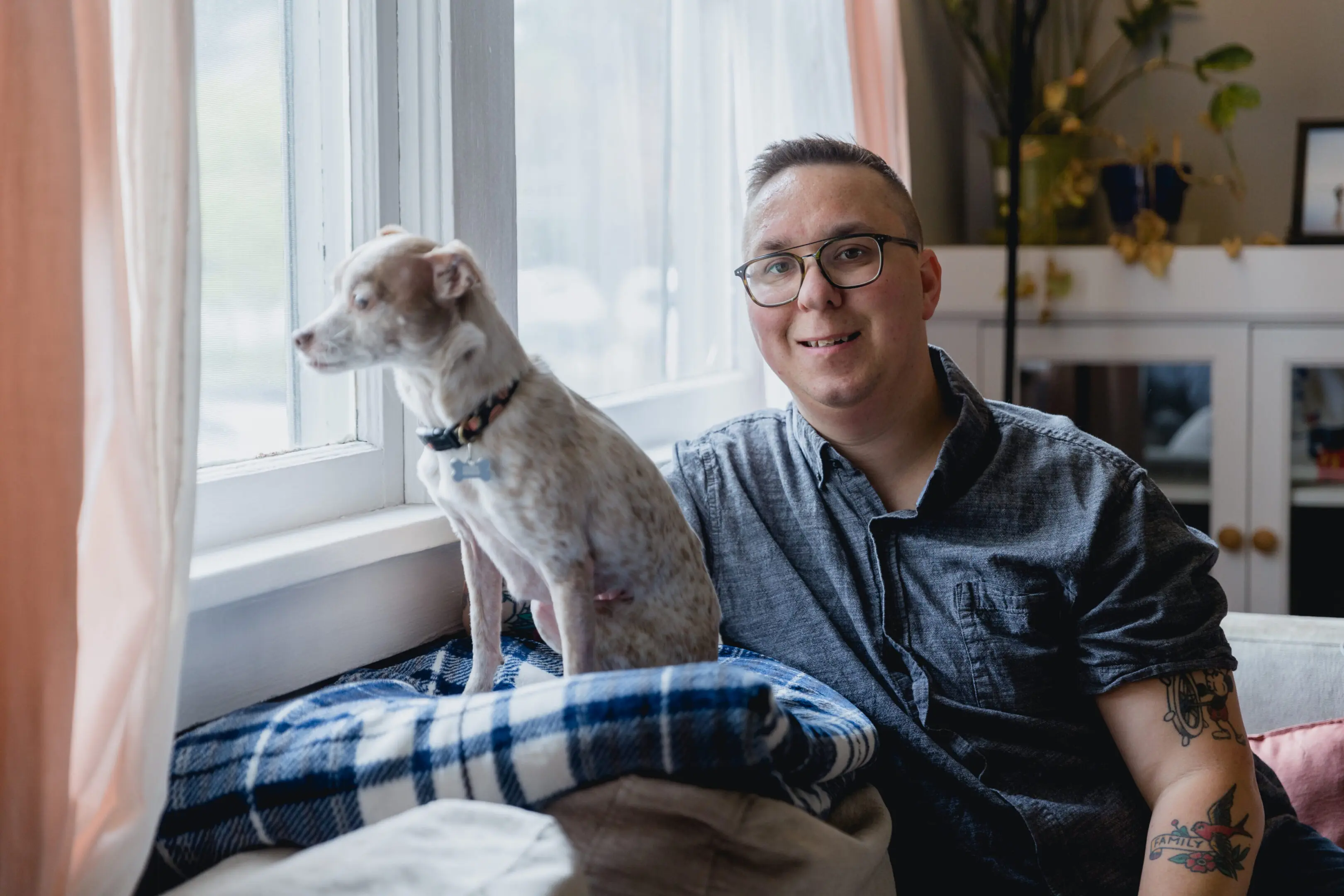 Man smiling next to a small dog by a window.