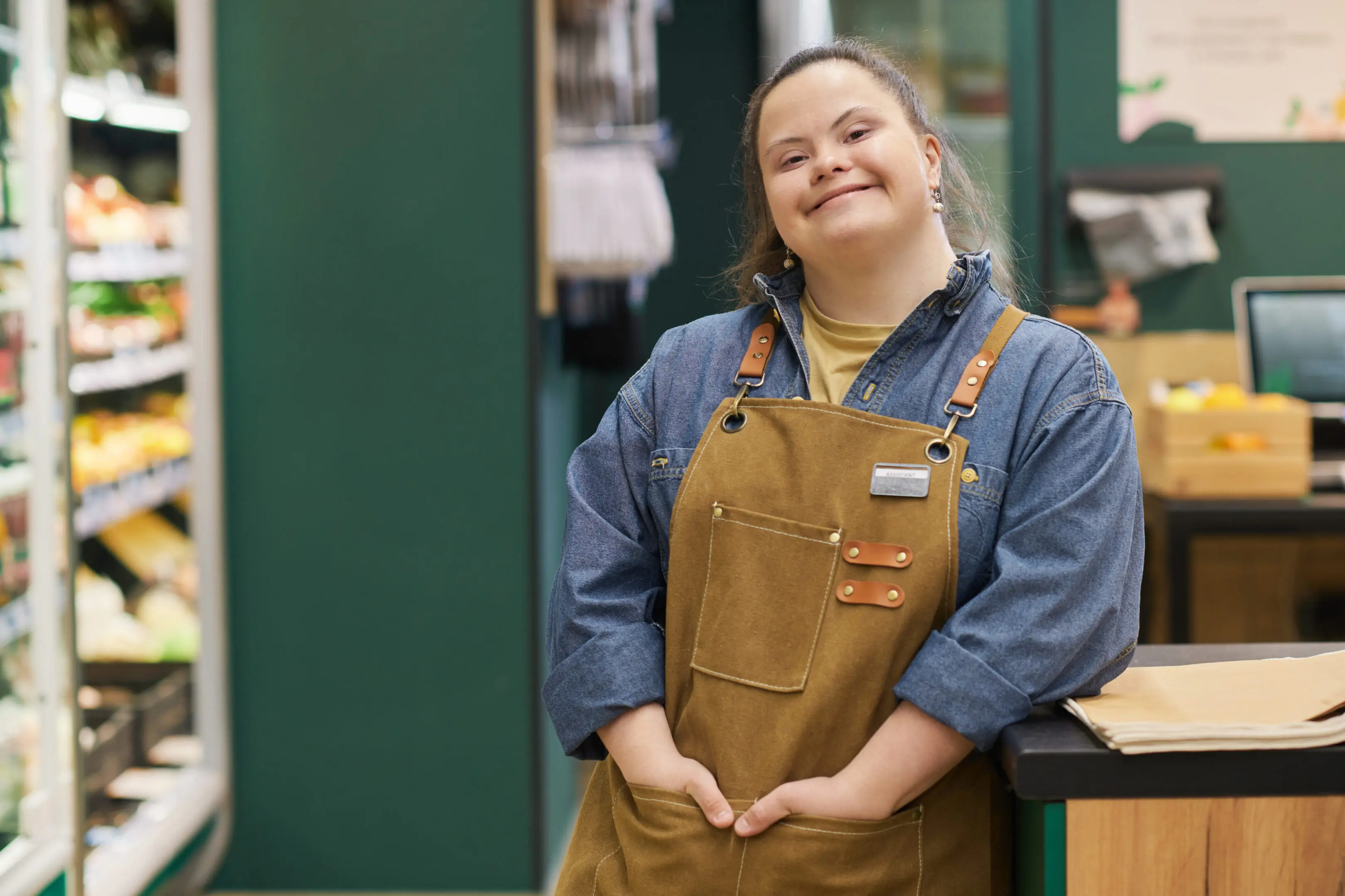 Smiling woman with Down syndrome in apron stands confidently indoors.