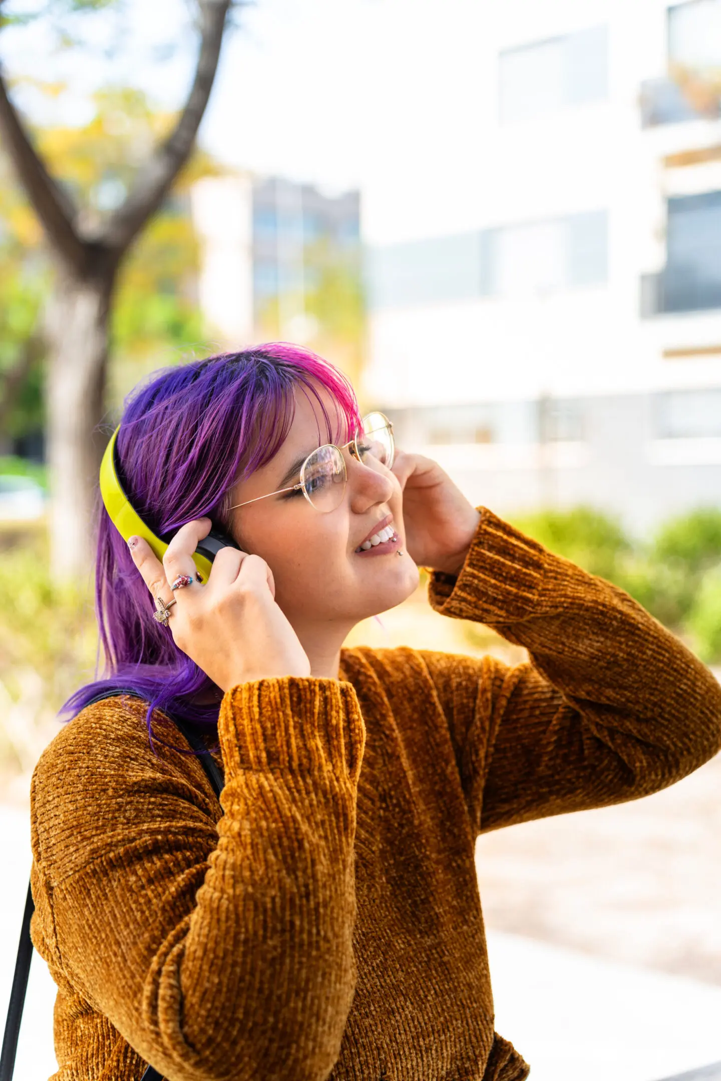 Young woman with purple hair enjoying music outdoors with headphones.