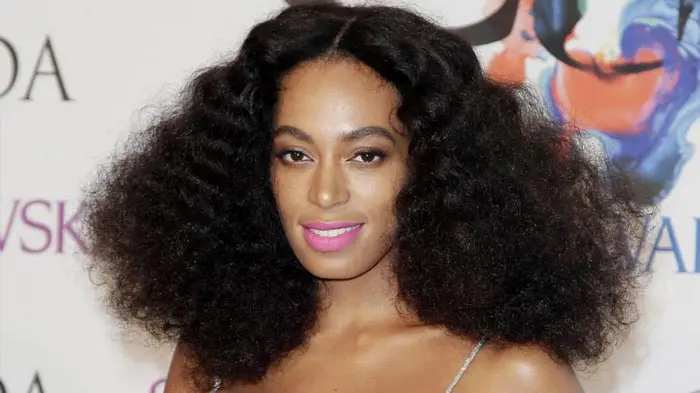 Woman with voluminous curly hair and pink lipstick smiles at the camera.