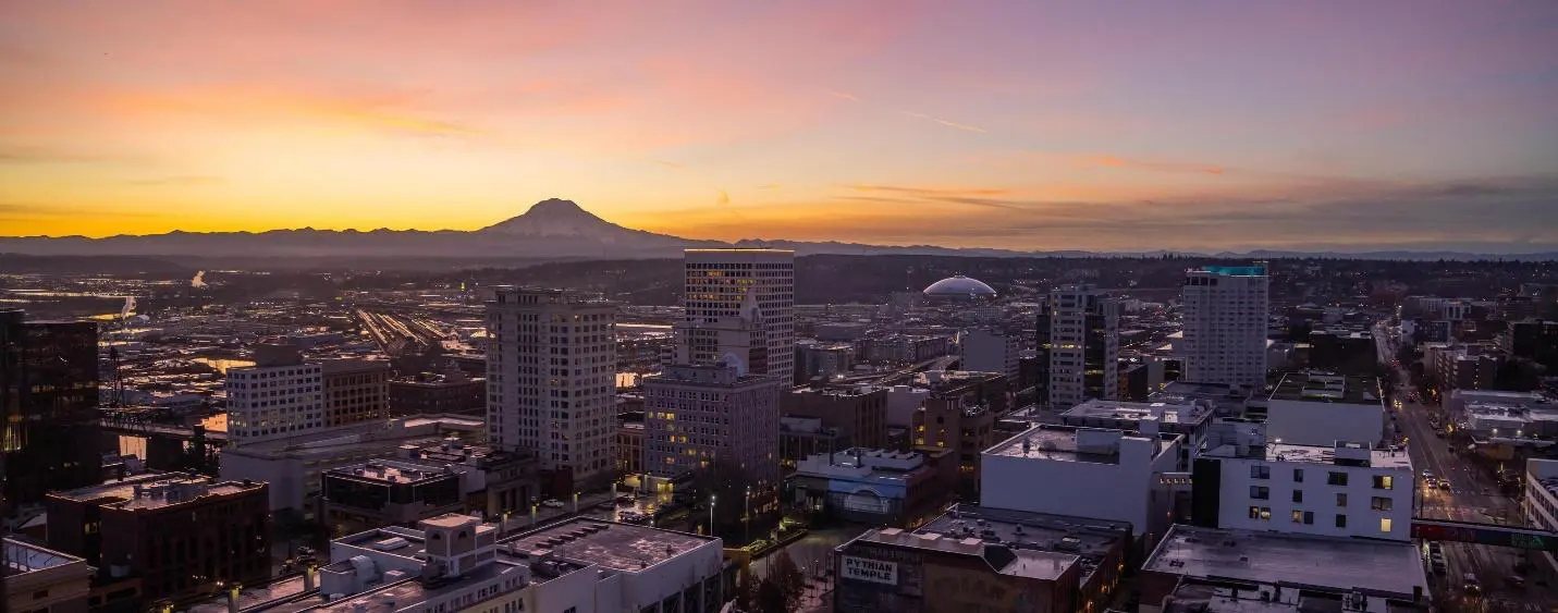 Sunset over a city skyline with a mountain in the background.