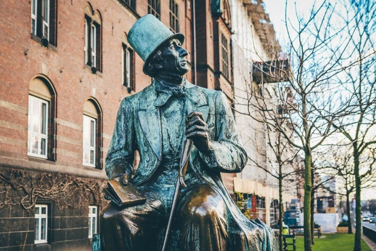 Statue of a man with a top hat sitting on a bench outdoors.