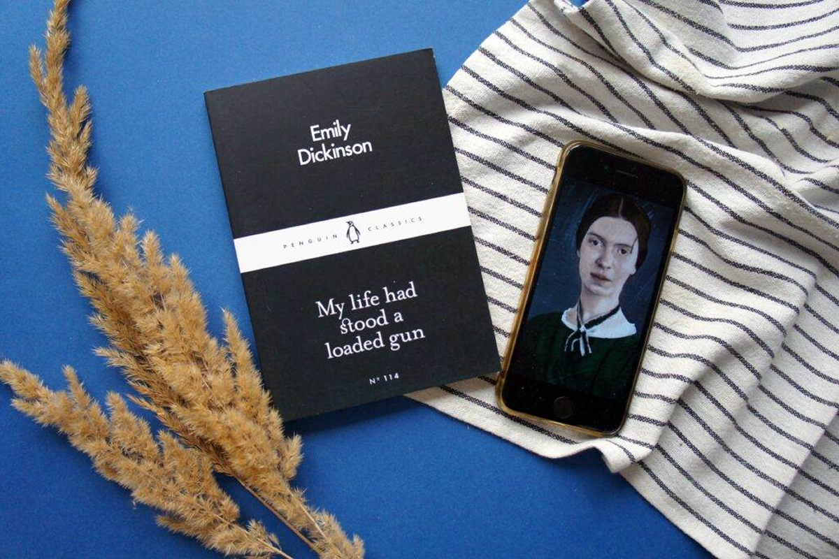 A phone displaying a person's photo beside a book of Emily Dickinson poems.